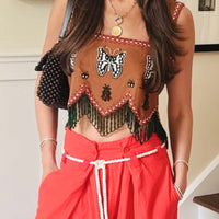 Woman in a stylish outfit with a top and red pants standing in a home setting wearing the pave diamond necklace with hipV locket.