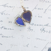 Heart-shaped blue pendant on a gold chain against a background of handwritten text.