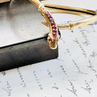 Angled view of a vintage gold snake bracelet showcasing the sculpted serpent head and ruby-set crest.