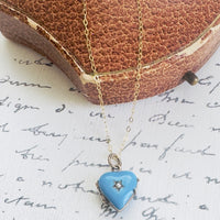 Gold necklace with a blue heart-shaped pendant on a textured surface with text.