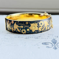 Front view of oval vintage hinged bangle with gold floral detailing on a dark ground