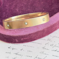 Gold filled bangle bracelet showing three starbursts with seed pearls