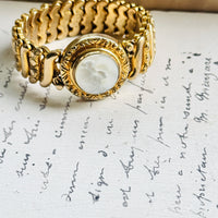 Gloria sweetheart bracelet with white Lucite medallion and wide gold filled expansion band, styled on a handwritten letter