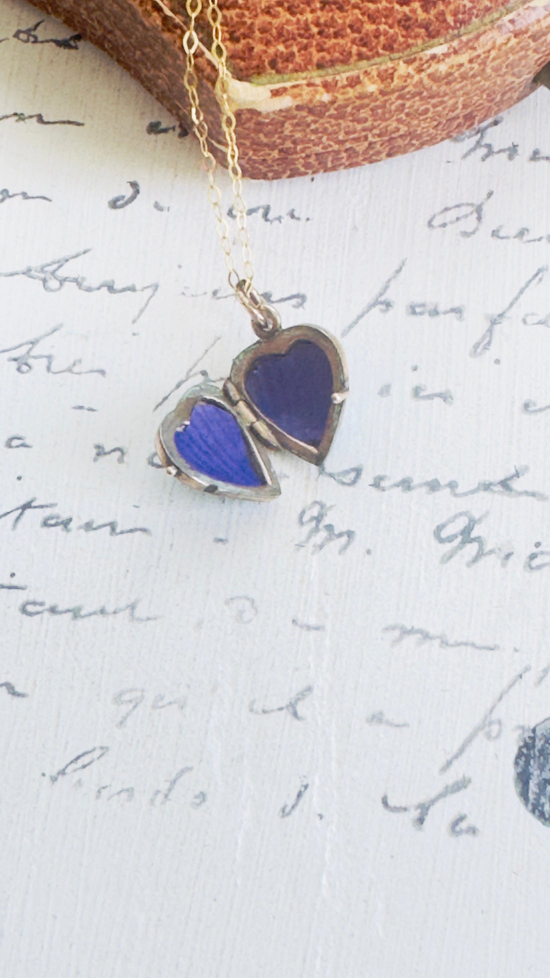 Heart-shaped blue pendant on a gold chain against a background of handwritten text.