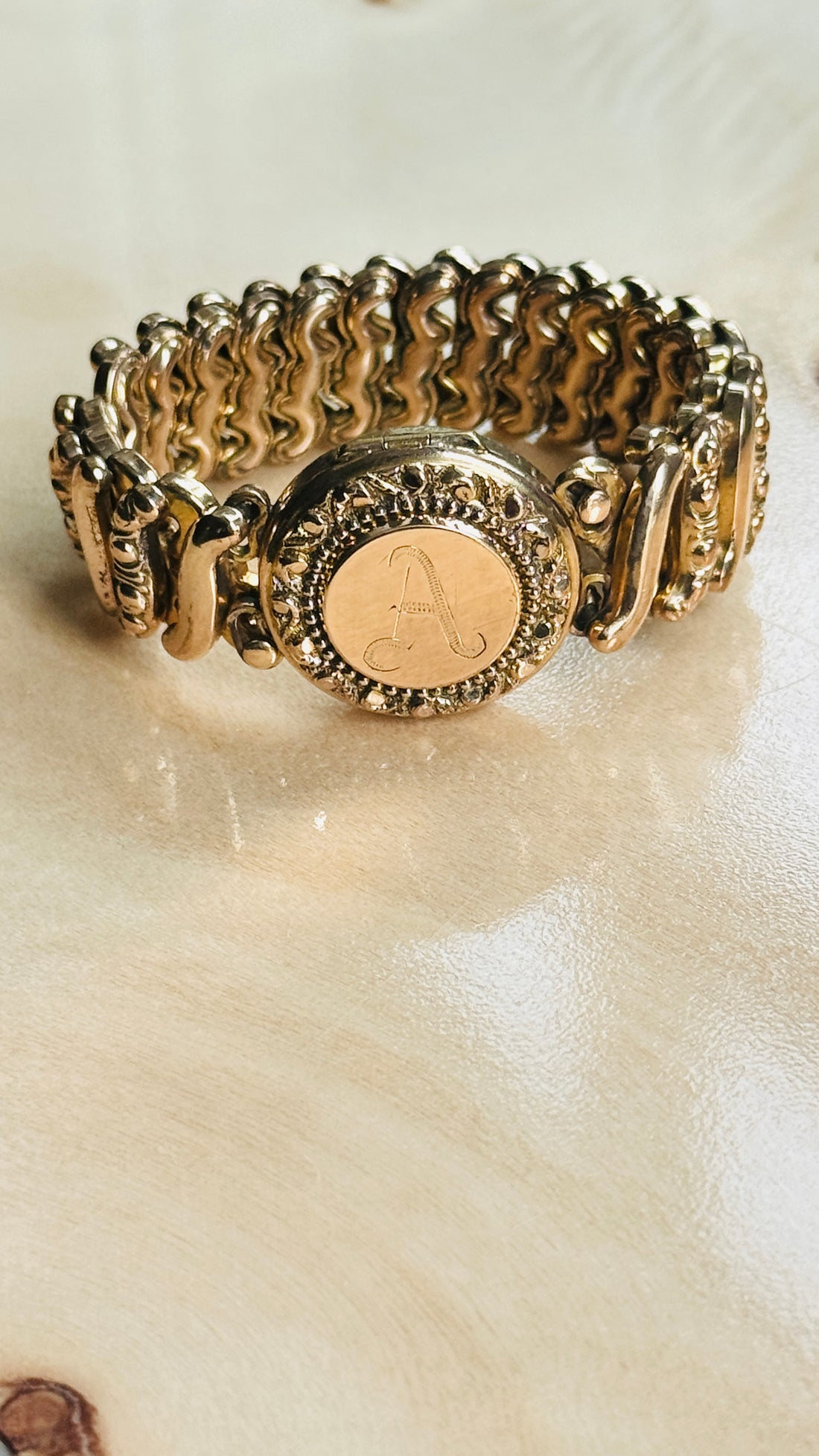 Angled view of a vintage Carmen gold-filled sweetheart expansion bracelet with engraved monogram locket.