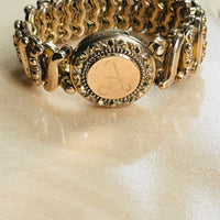 Angled view of a vintage Carmen gold-filled sweetheart expansion bracelet with engraved monogram locket.