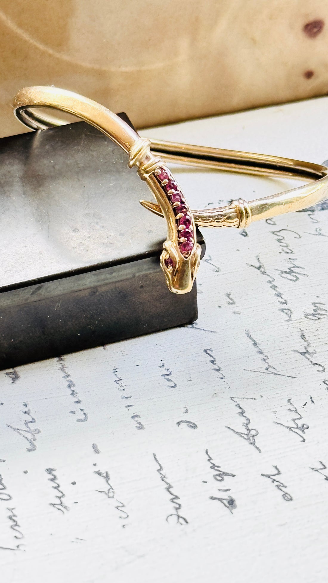 Angled view of a vintage gold snake bracelet showcasing the sculpted serpent head and ruby-set crest.