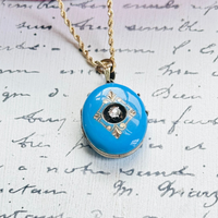 Blue enamel diamond locket on 14k gold chain styled on handwritten paper background.