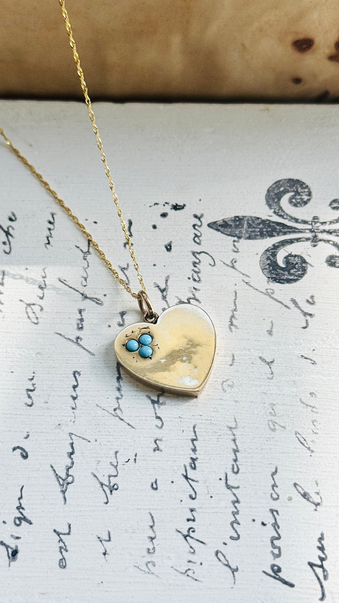 Antique 9ct gold heart pendant necklace styled on a vintage manuscript background.
