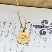 Antique French FIX cherub medal styled on a gold chain over vintage handwritten paper.