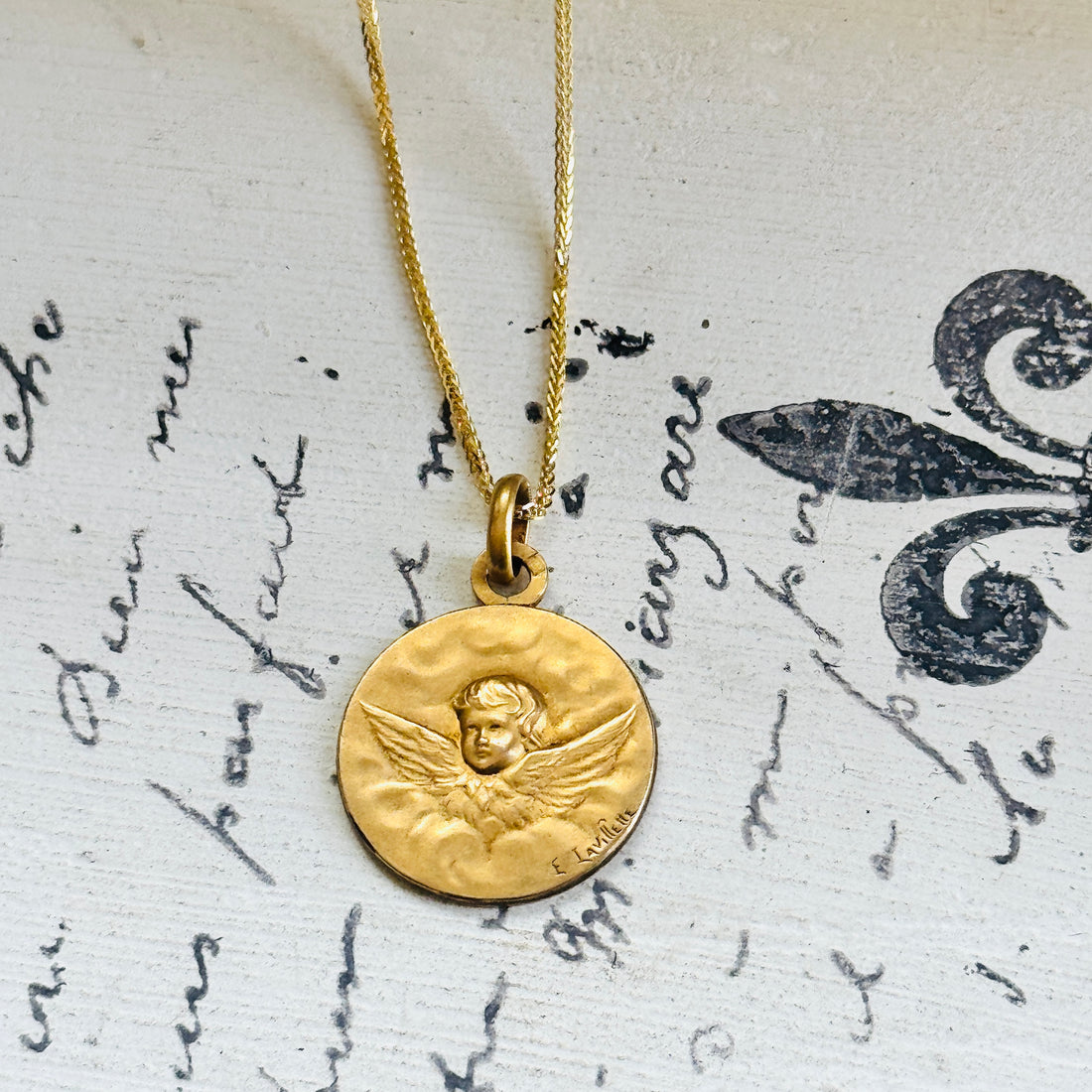 Antique French Art Nouveau cherub medal by E. Lavilette on a 10k gold chain, styled over vintage script paper.