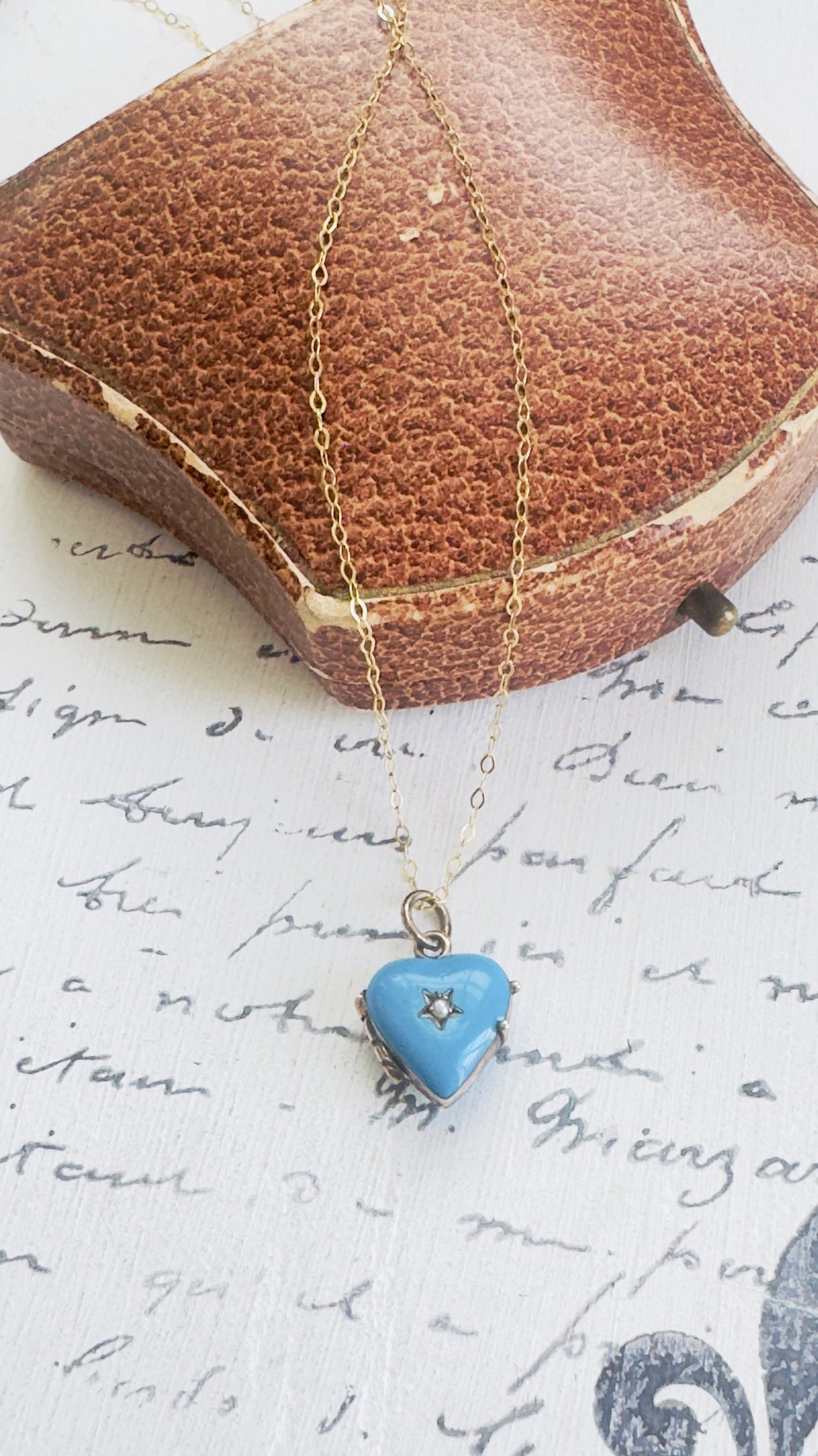 Gold necklace with a blue heart-shaped pendant on a textured surface with text.