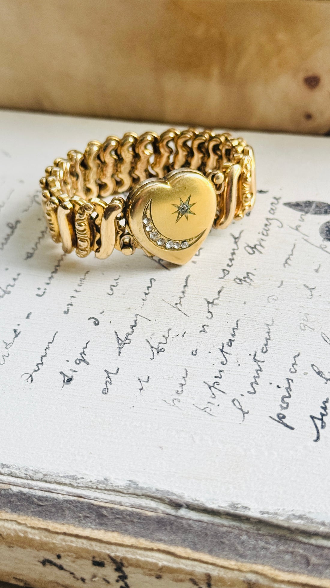 Carmen gold-filled sweetheart locket bracelet displayed on antique handwritten paper, showing its celestial moon and star design
