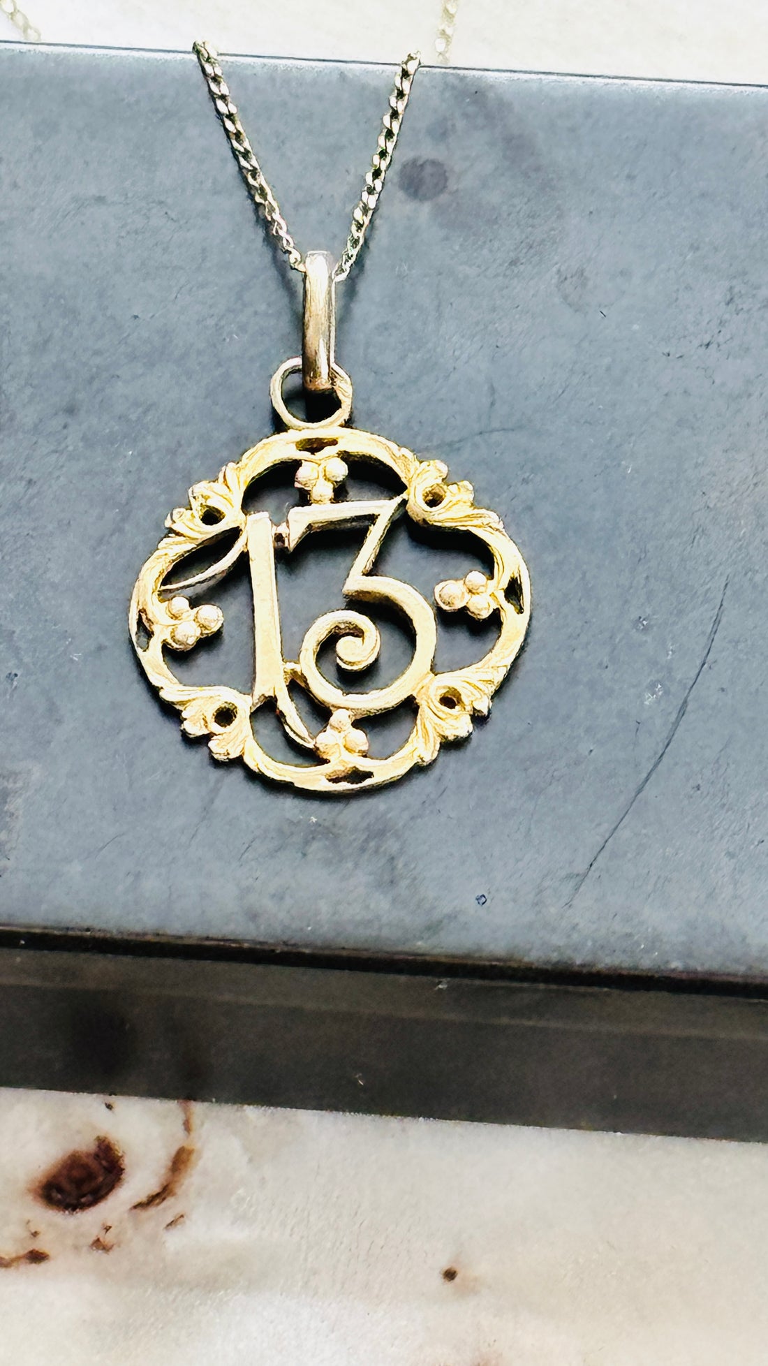 Close-up of an antique French Lucky Number 13 pendant in solid 18k gold suspended from a 14k gold chain.