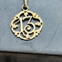 Close-up of an antique French Lucky Number 13 pendant in solid 18k gold suspended from a 14k gold chain.