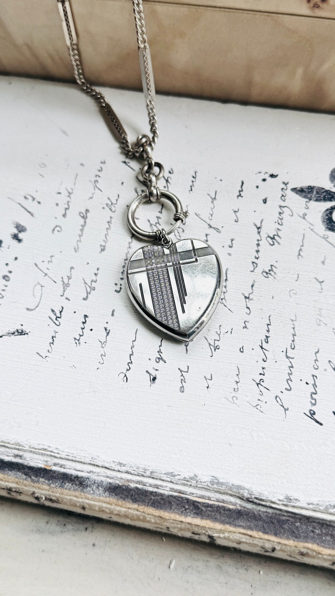 Close-up of an antique sterling silver Art Deco heart locket pendant styled on an antique watch chain.