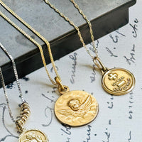 Collection featuring an original Alphonse Augis French Love Token alongside two antique cherub pendants in 18k gold.