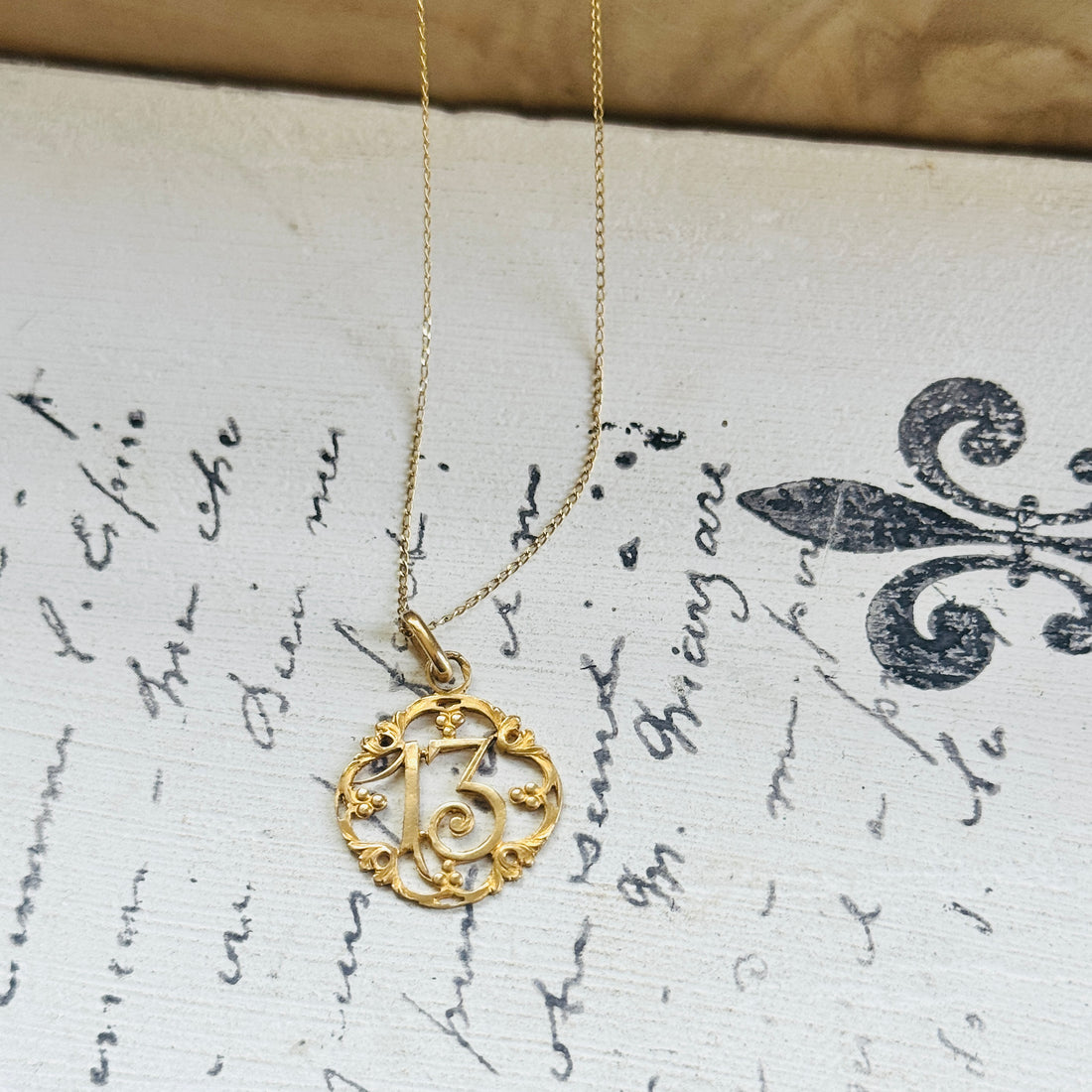 French Lucky Number 13 charm pendant displayed on handwritten paper, featuring an openwork 18k gold design and French eagle's head hallmark.