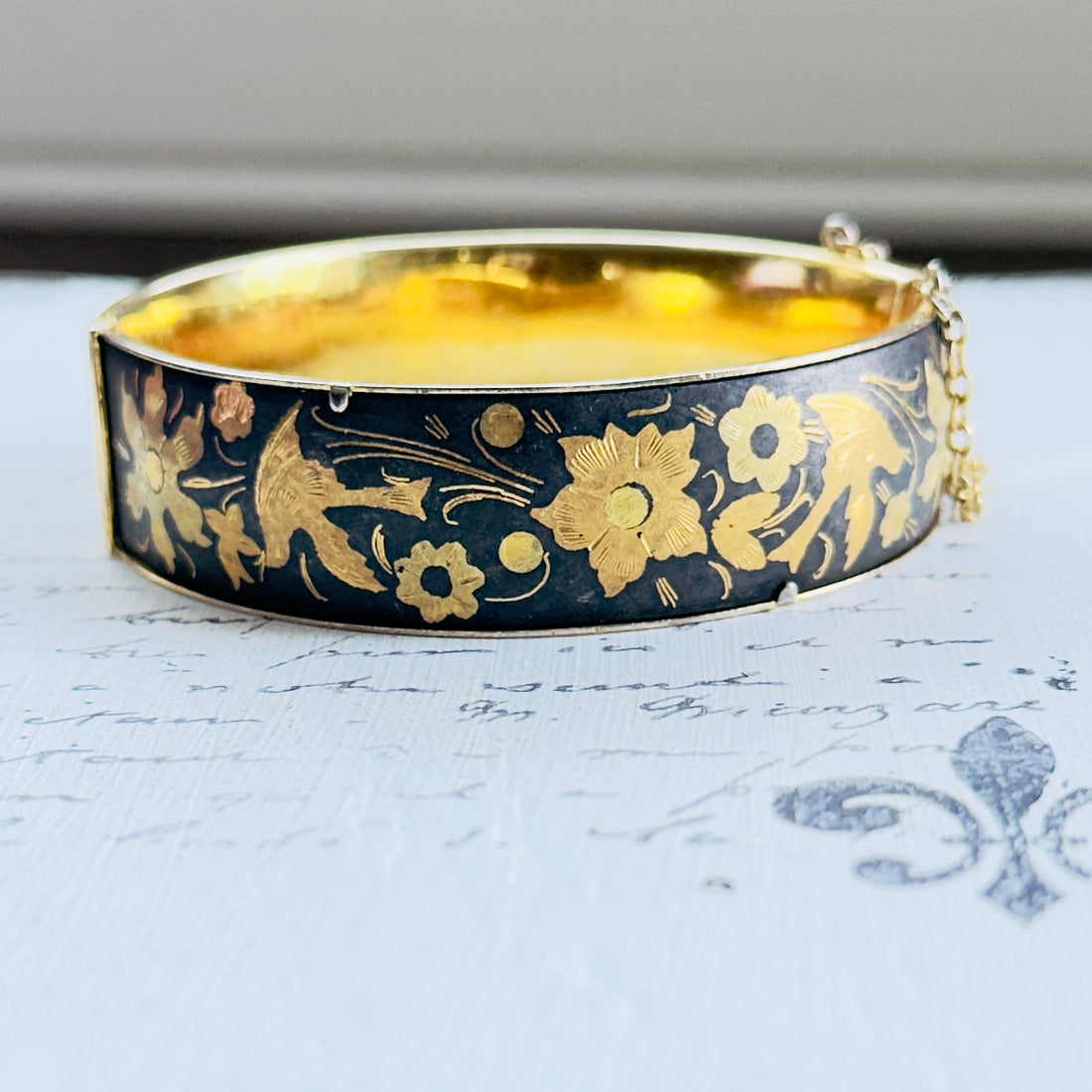 Front view of oval vintage hinged bangle with gold floral detailing on a dark ground
