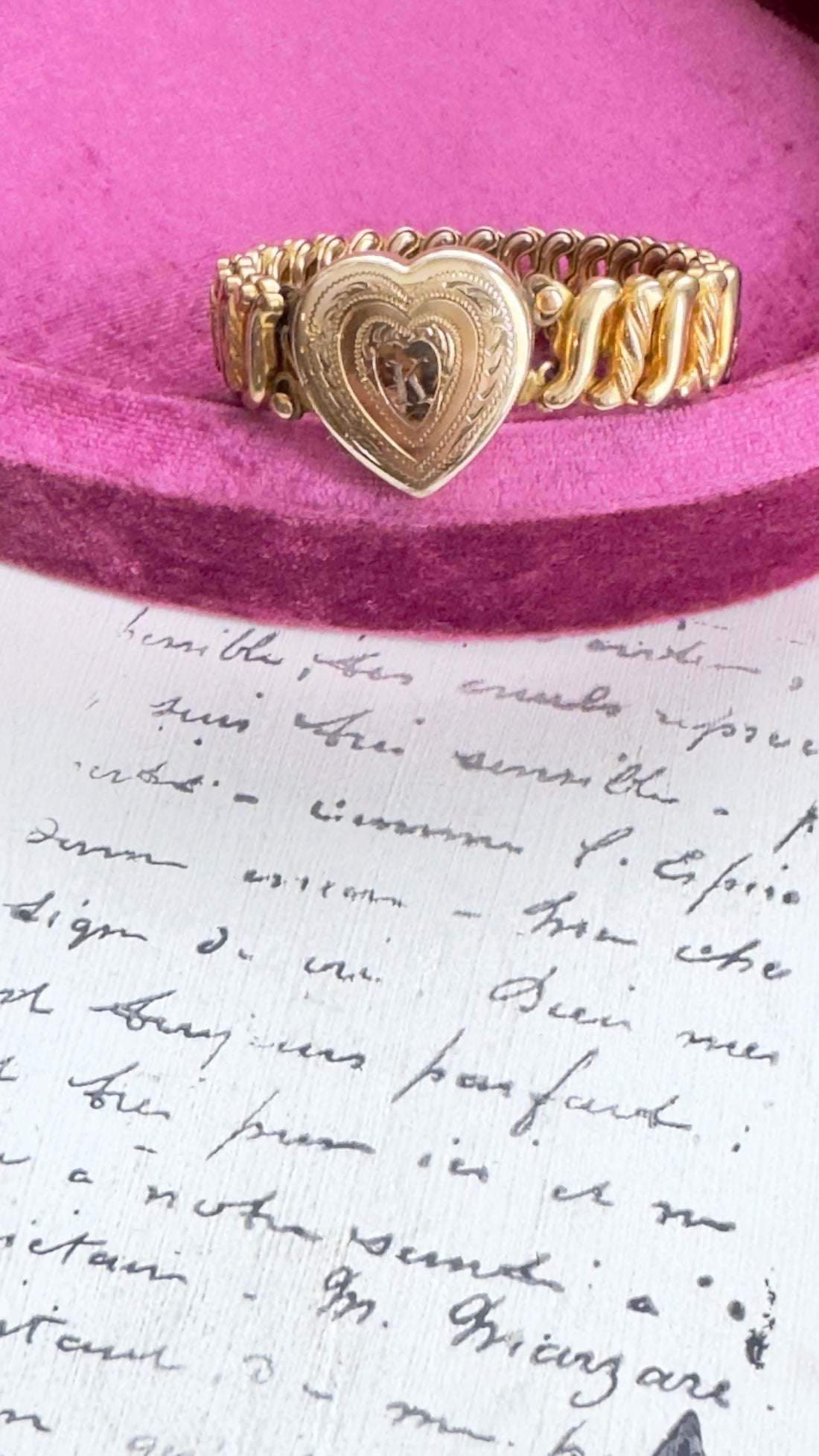 Close-up of engraved heart locket with floral scroll detailing on vintage gold bracelet.