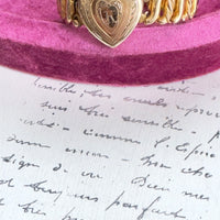 Close-up of engraved heart locket with floral scroll detailing on vintage gold bracelet.