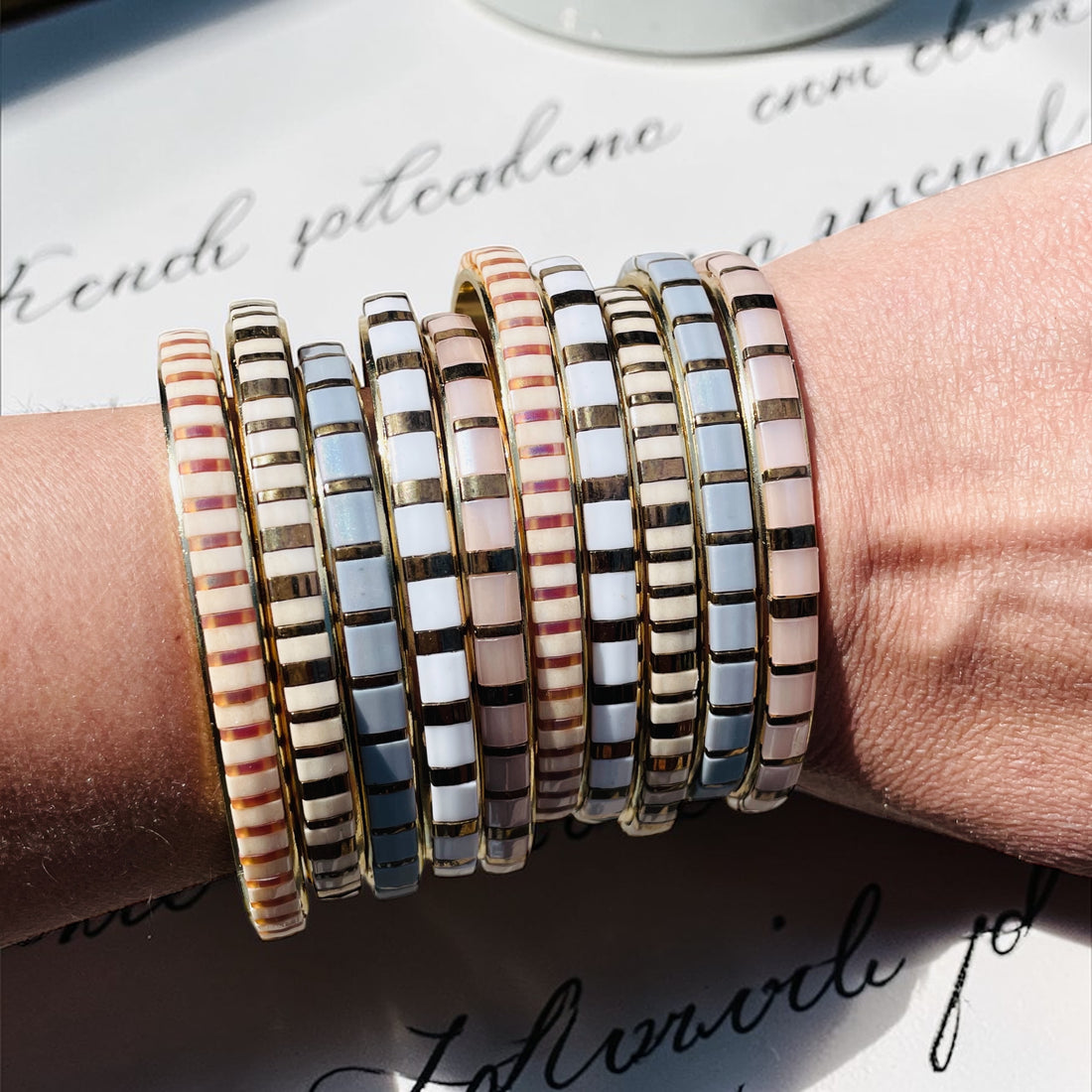 Stack of modern glass tile bracelets on wrist in mixed neutral tones