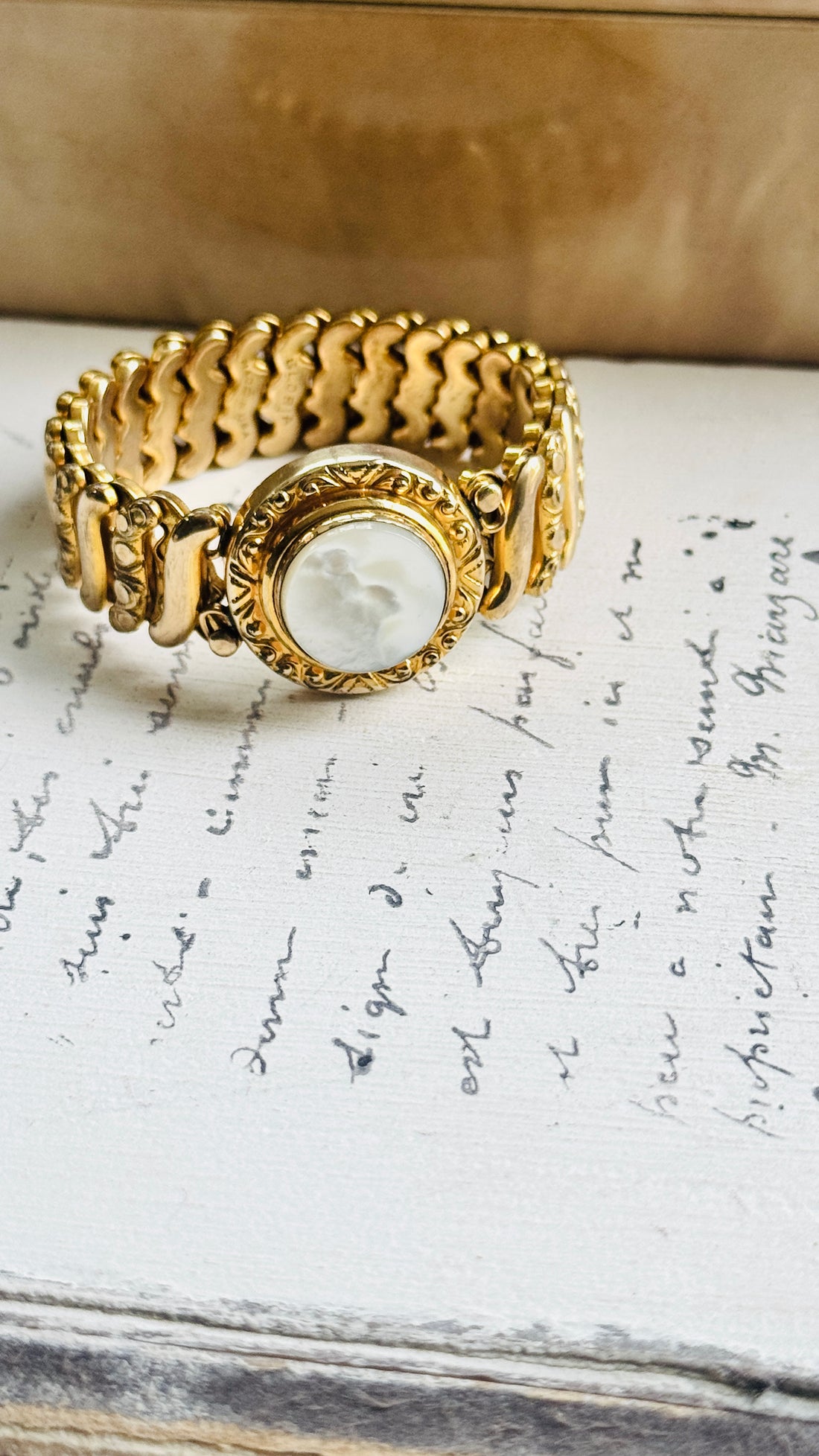 Gloria sweetheart bracelet with white Lucite medallion and wide gold filled expansion band, styled on a handwritten letter
