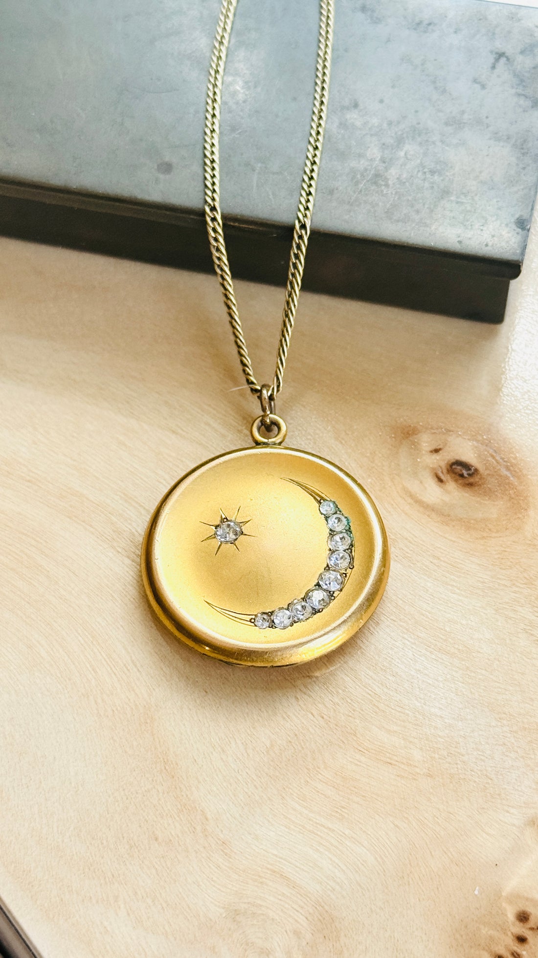 Gold filled crescent moon and star locket hanging from its chain, set with paste stones